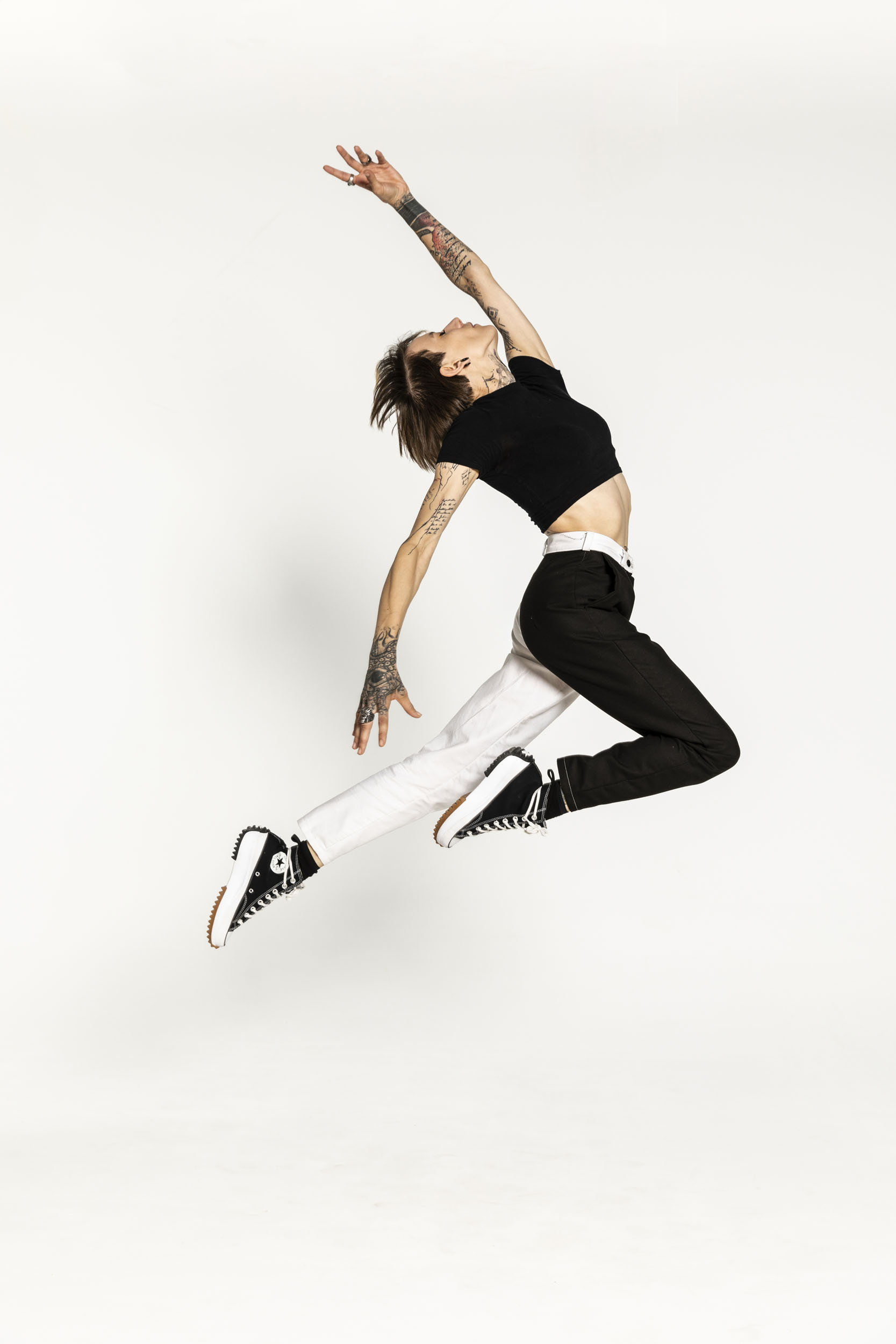 Portrait artistique d'une jeune femme tatouée qui réalise un saut devant un fond blanc. Photo de plain-pied réalisée en studio pour la banque d'images  Plainpicture.