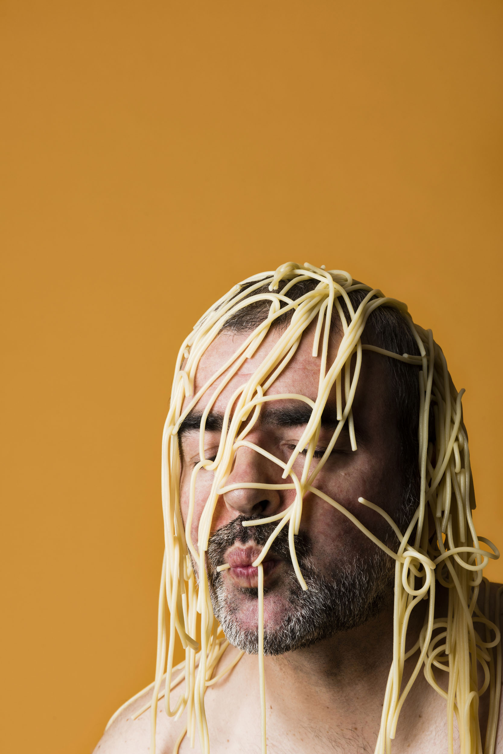 Portrait artistique d'un homme torse nu avec des spaghettis cuits sur la tête. Photo de portrait réalisée en studio pour la banque d'images  Plainpicture.