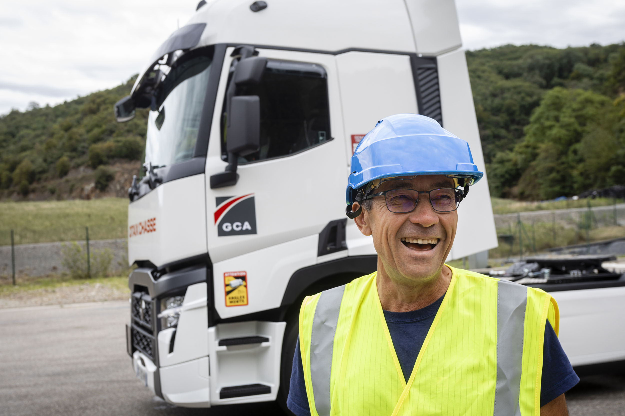 Portrait d'un chauffeur souriant devant son tracteur routier sur le site d'une entreprise. Photo de portrait réalisée pour le Groupe Charles André.
