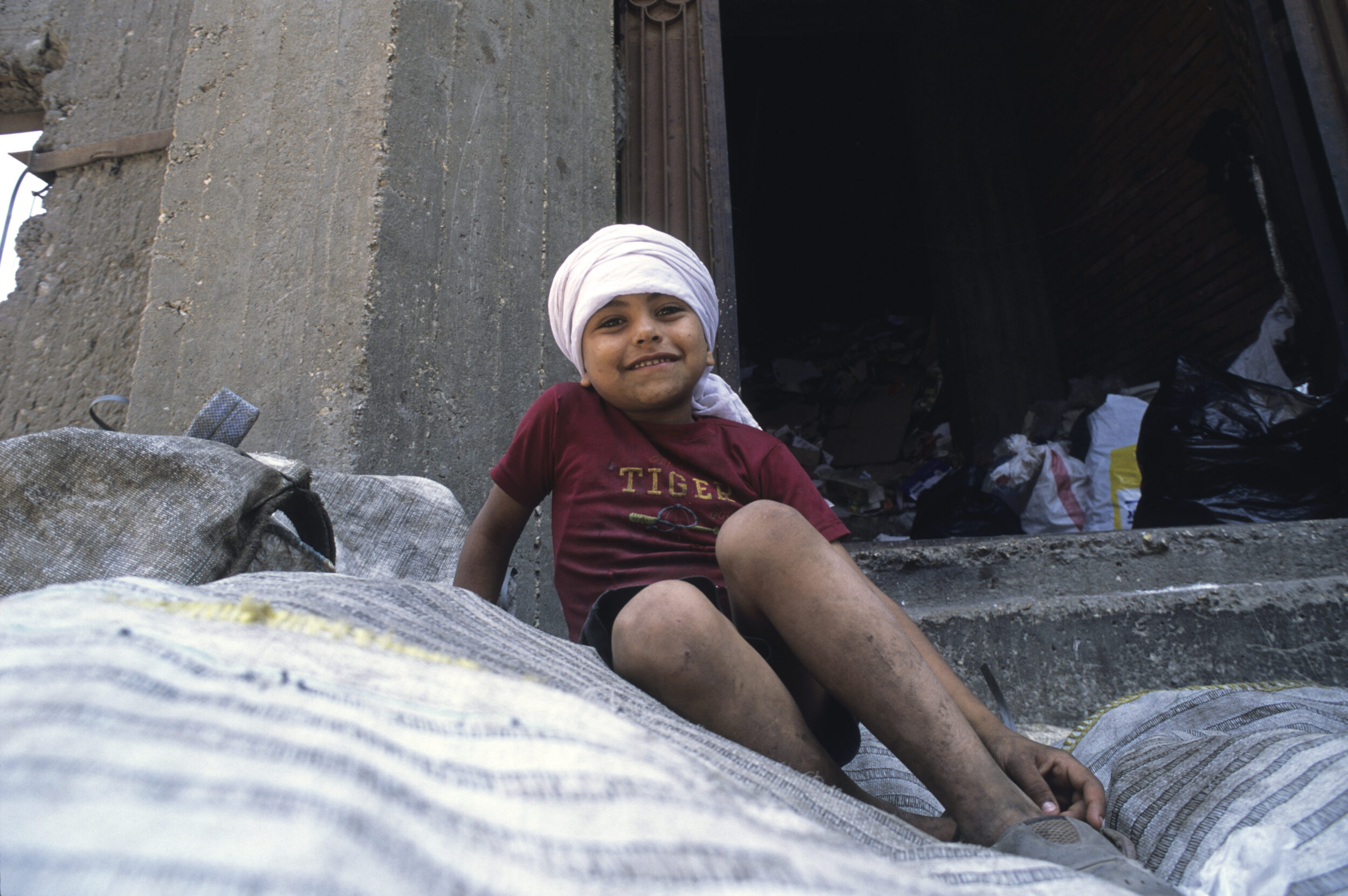 Photo de portrait d'un jeune Zabbal souriant posant sur un tas de sacs remplis de déchets triés valorisables.