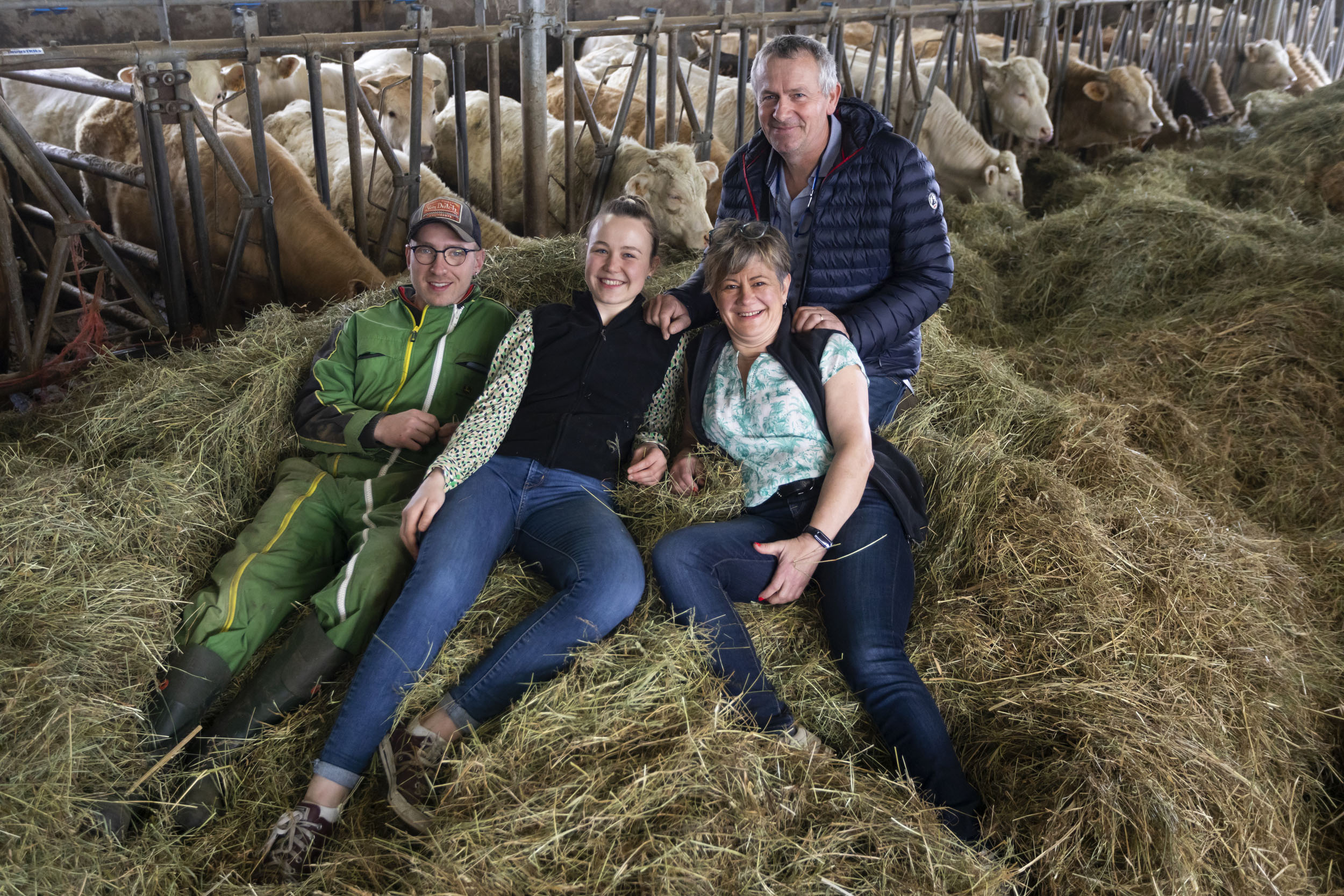 Portrait d'une famille d'éleveurs heureuse  qui pose dans le foin au milieu de l'étable. Photo de portraits commandée par la société Cerfrance.