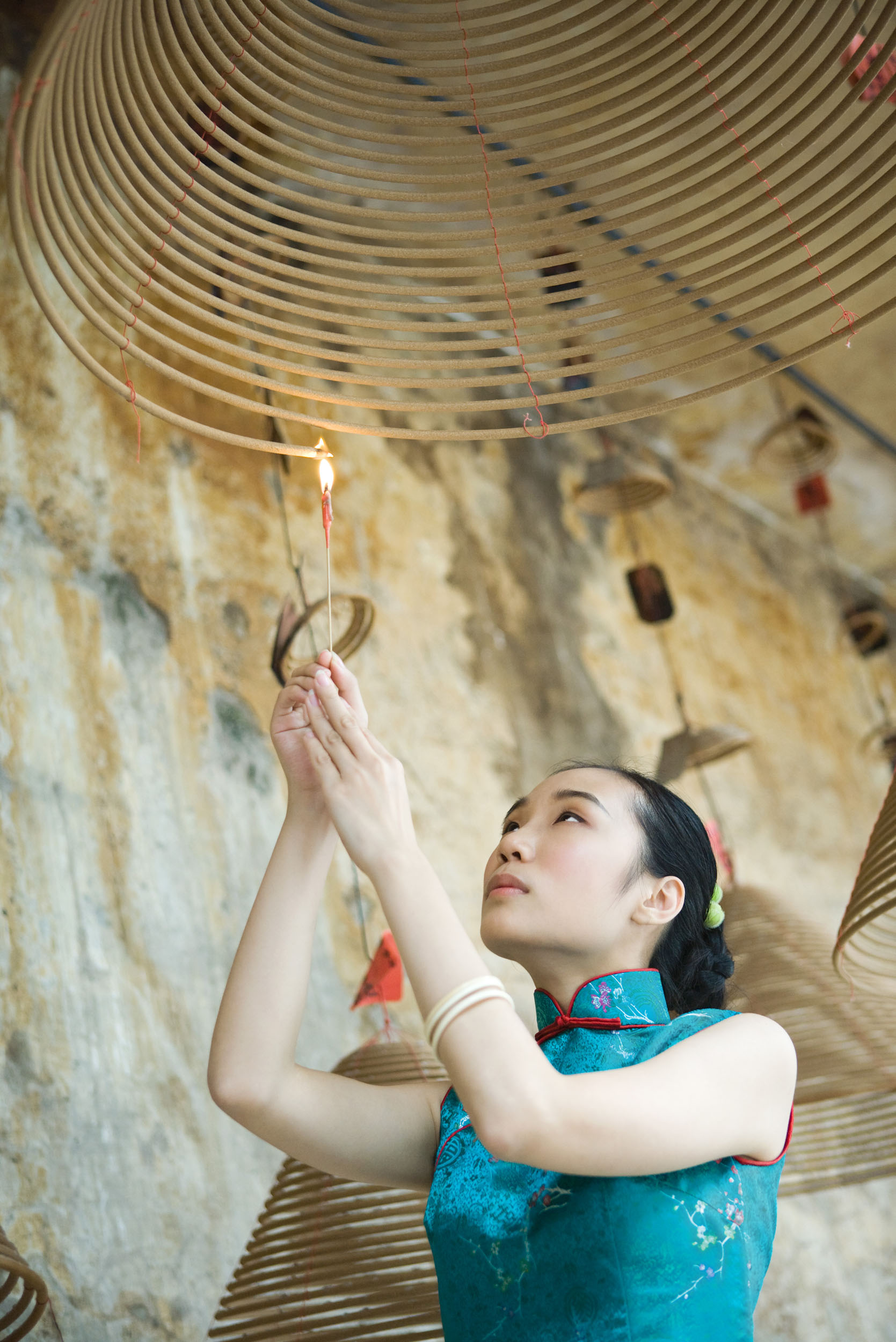 Portrait en lumière naturelle d'une femme asiatique qui allume une bobine d'encens dans un temple. Photo de portrait en contre plongée.