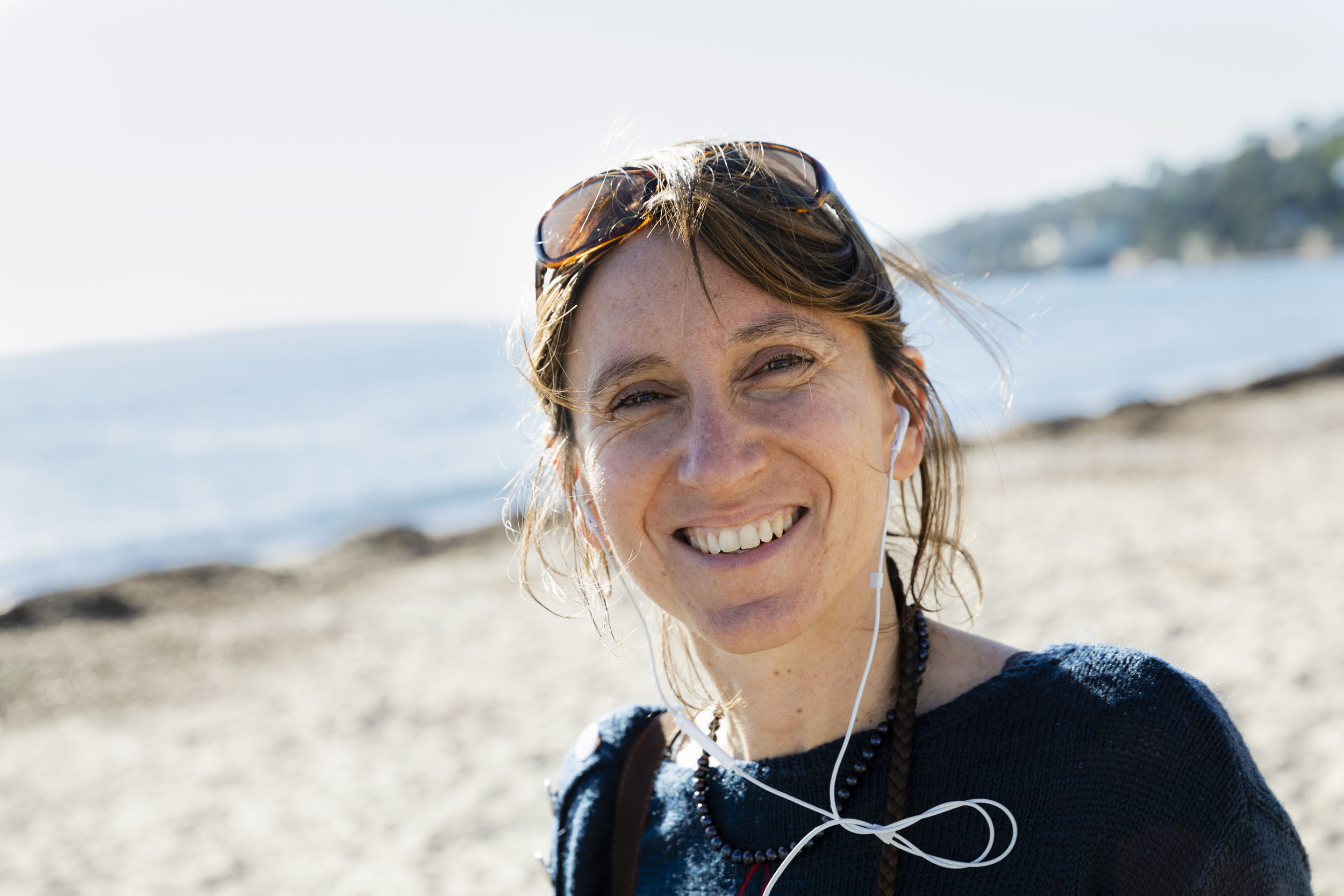 Portrait de vie d'une femme souriante sur une plage en hiver avec ses écouteurs de portable aux oreilles. Photo de portrait réalisée pour la banque d'images Plainpicture.