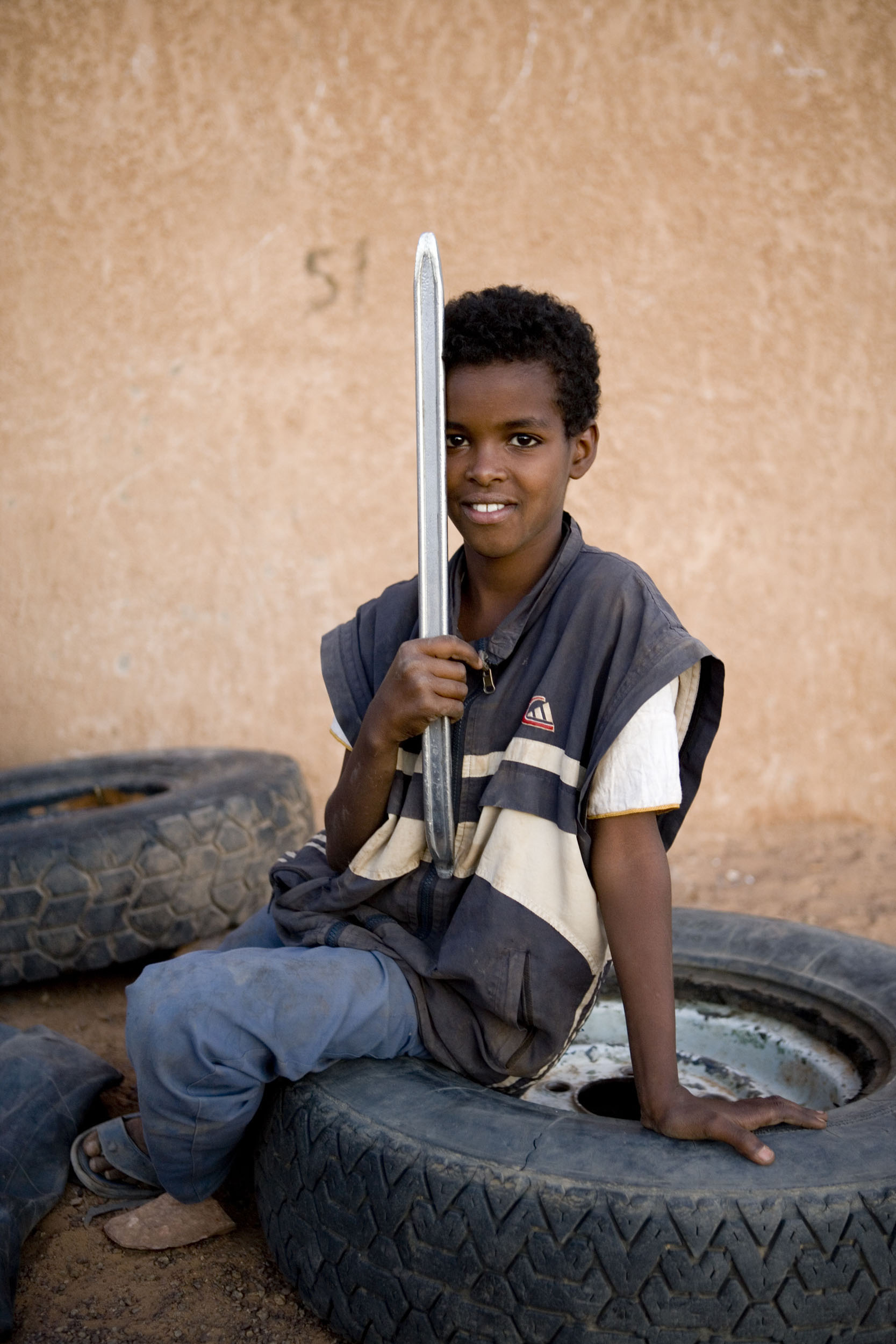 Portrait d'un enfant assis sur un gros pneu de camion avec un démonte pneu à la main. Photo réalisé dans la rue lors d'un voyage en Mauritanie.