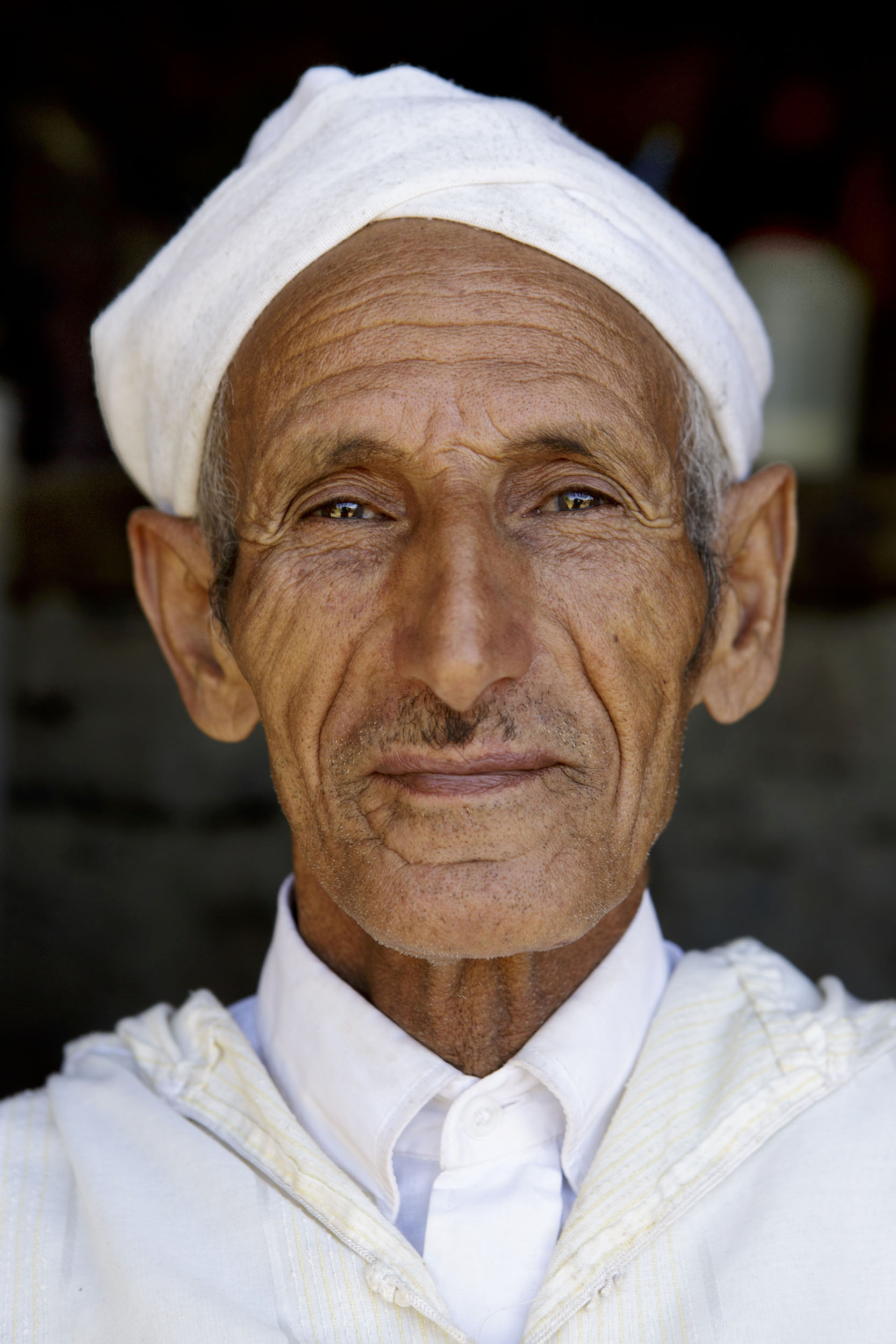 Portrait posé d'un homme en chemise blanche, djellaba et chèche blanc sur la tête réalisé dans la vallée d'Anergui au Maroc.