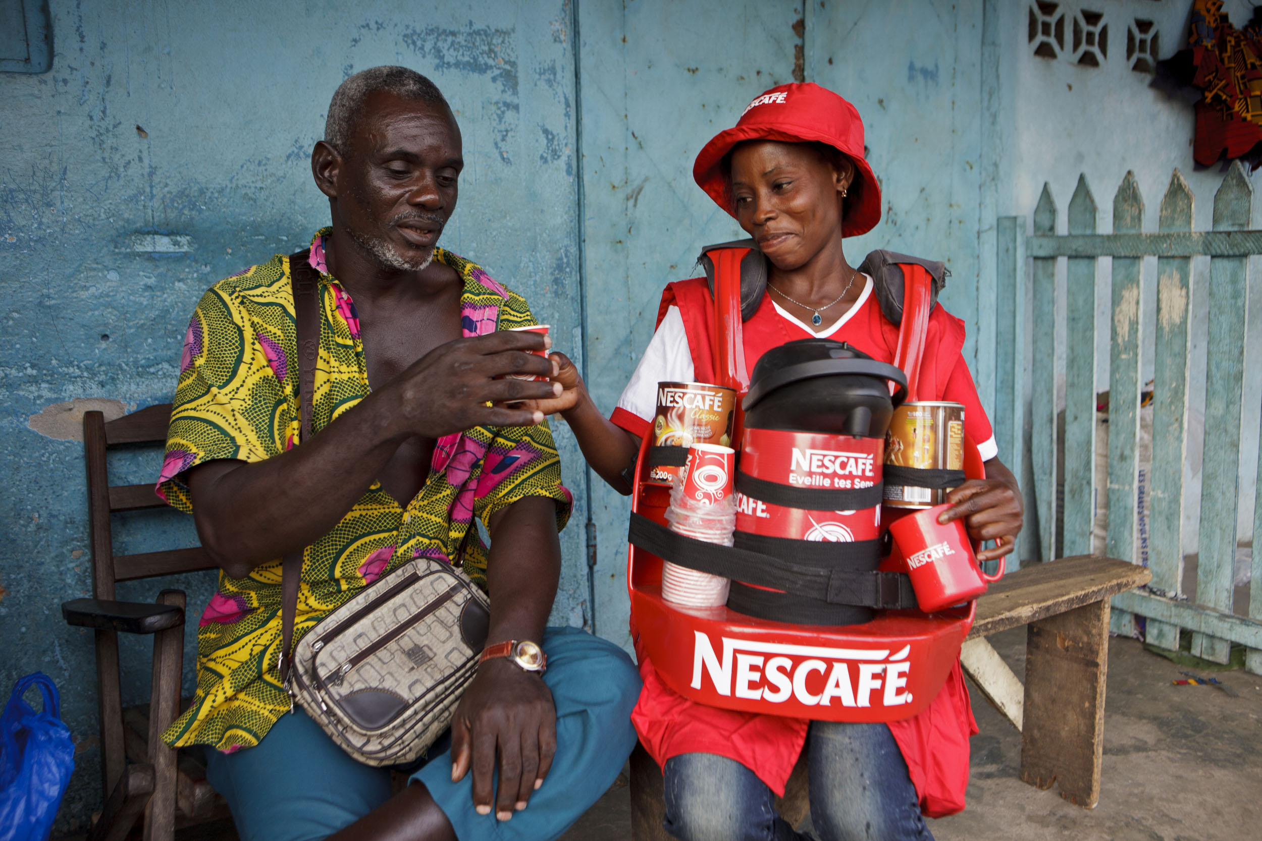 Portrait de vie quotidienne d'une marchande ambulante Myowbu (My Own Business) avec son client sur un marché en Côte d'Ivoire. Photo de portraits en reportage commandé par la marque  Nescafé® du Groupe Nestlé®.